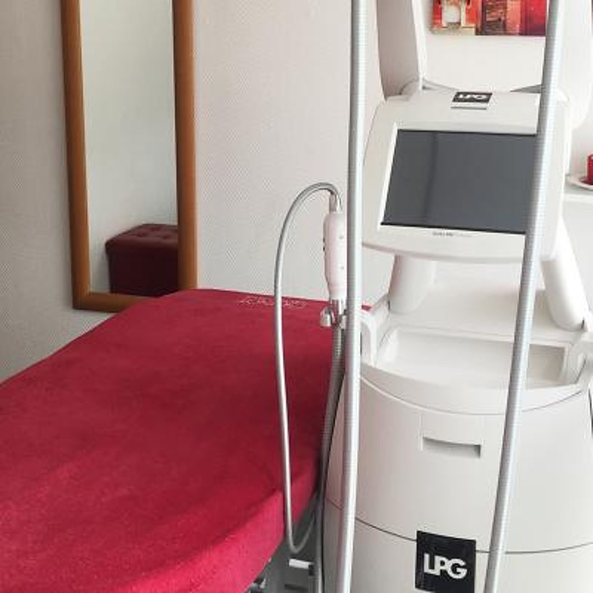 Un appareil LPG avec écran tactile et manipulateur se trouve dans une cabine de soin, à côté d'une table recouverte d'une serviette rouge et d'un miroir au cadre en bois.