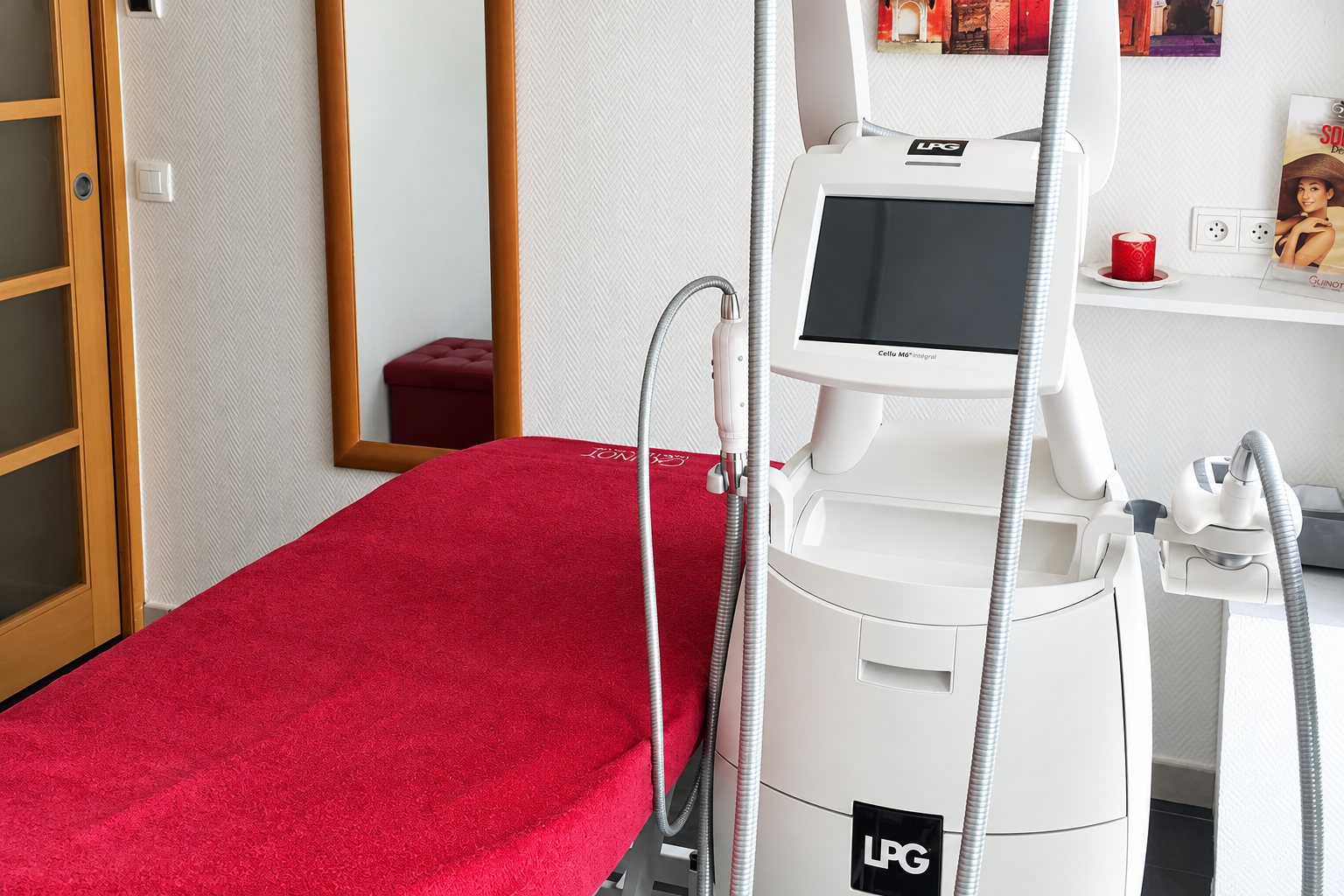Une cabine de soins esthétiques équipée d'un appareil LPG blanc à écran, à côté d'une table recouverte d'une serviette rouge.
