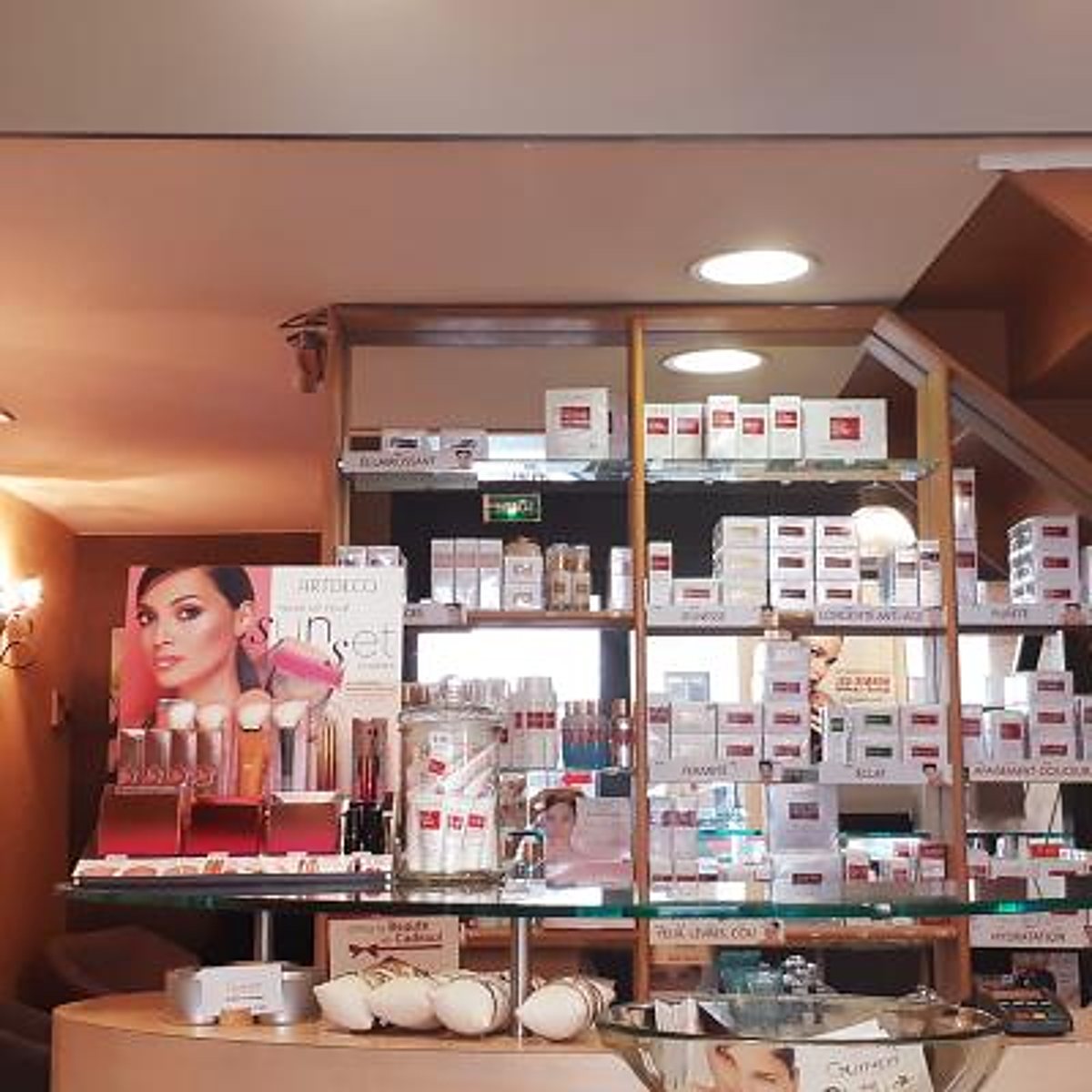 Étagères vitrées d'un institut de beauté présentant des crèmes, des pinceaux de maquillage et une affiche publicitaire Artdeco.